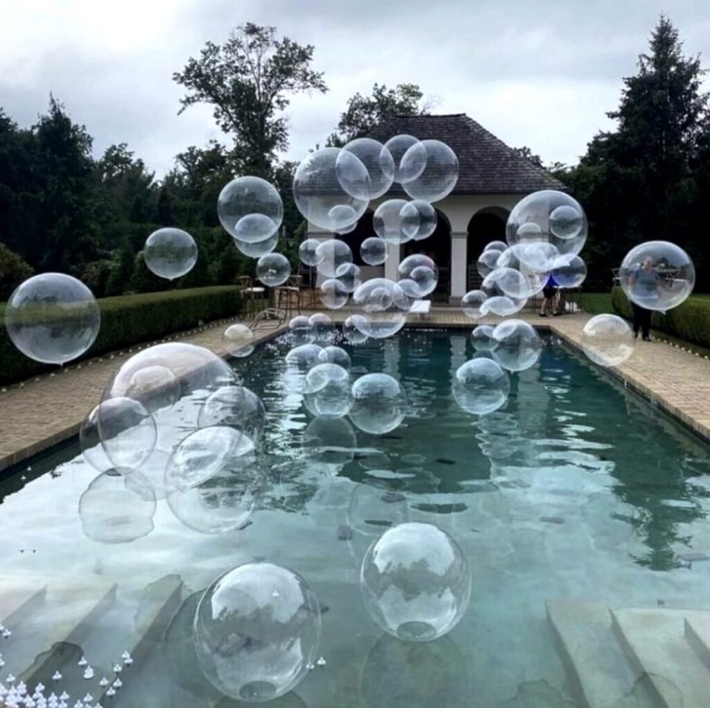 Balloon decorations for parties and events. Clear bubble orb balloons floating over pool for party.